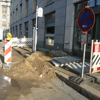 Fußgänger laufen ungeregelt in den Sandhaufen an einer Gehwegbaustelle.