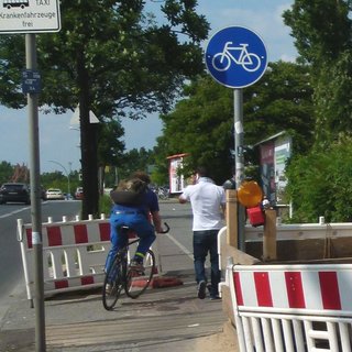 Fußgänger und Radfahrer drängeln sich auf einer Baustellen-Umgehung.