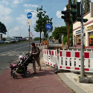 Fußgängerin mit Kinderwagen versucht, über die Fahrbahn zu kommen.